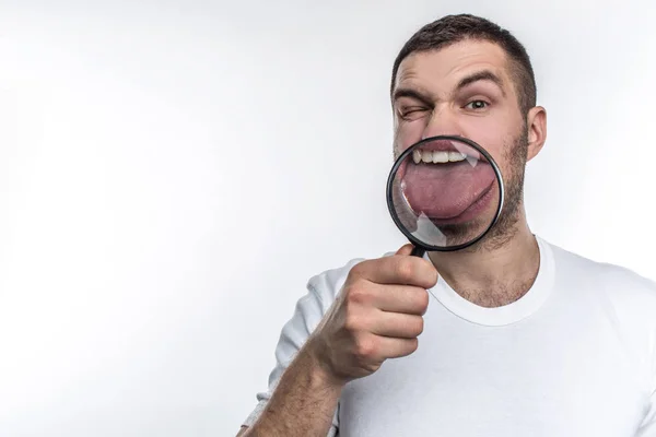 Man with magnifying glass is looking straight ahead and showing his tongue through the glass. Isolated on white background. — Stock Photo, Image