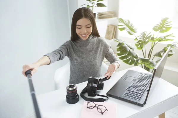 Das dunkelhaarige Mädchen sitzt am Tisch und streamt ein Video. zeigt sie ihren Followern ihre Ausrüstung für Fotoshootings. sie ist aufgeregt und glücklich. — Stockfoto