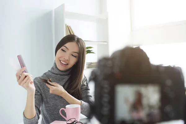 Diese Beauty-Bloggerin nimmt ein Video über Haarpflege und Haarspitzen auf. Sie schaut zu der Haarbürste, die sie empfiehlt. Es gibt auch eine Kamera auf einem Bild. — Stockfoto