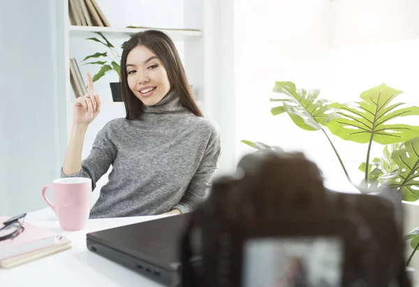Beutiful blogger is sitting at the table and pointing up. She is recording on camera new video for her youtube account. — Stock Photo, Image