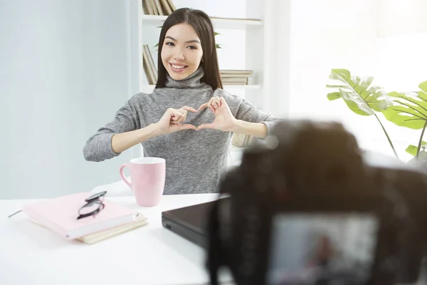 Erstaunliche und hinreißende Mädchen zeigt ein Herz in die Kamera. Sie hält ihre Hände dicht vor der Brust und lächelt. diese unglaubliche junge Frau sieht glücklich aus. — Stockfoto