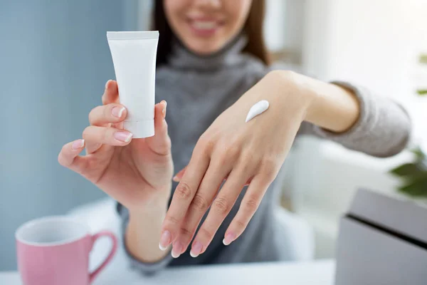 Gros plan des mains des filles. Elle tient un petit tube avec de la crème pour les mains dans une main et montre son autre main avec de la crème dessus. Le jeune blogueur sourit. Vue coupée . — Photo