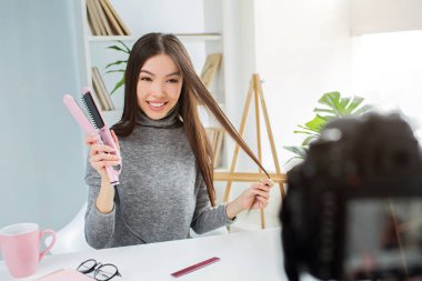 Güzel kız gülümseyerek ve kameraya bakıyor. O straitning saçlar için özel bir cihaz tutun. Bu aygıt için onun takipçileri tavsiye etmek istiyor.