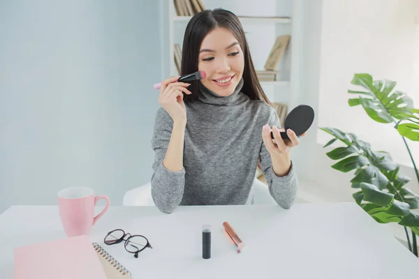 La blogueuse beauté se maquille. Elle a des coosmétiques sur la table. Fille regarde dans le miroir et souriant . — Photo