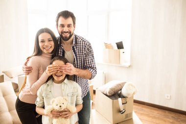 Güzel ve neşeli aile resmi. Genç anne Childs'ın gözünü ellerini tutuyor. Küçük kız tutmak bir kulak oyuncak ve gülümseyen.