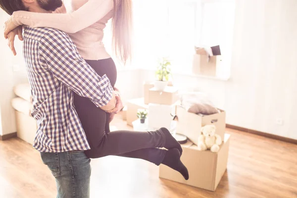 Nahaufnahme eines jungen Paares in einem hellen Raum. Der junge Mann hält seine Frau an den Händen. Auf dem Boden liegen Kisten mit verschiedenen Sachen. — Stockfoto
