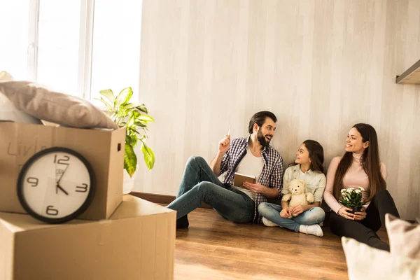 La joven familia está sentada junta en el suelo de la sala de estar. Acaban de mudarse a este apartamento. Las chicas buscan a un joven. Lo están escuchando. . — Foto de Stock