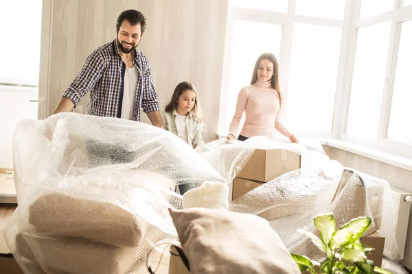 Famiglia bella e amichevole stanno disfacendo le valigie. Stanno rimandando la copertura delle scatole. Ci sono un sacco di cose li 'dentro. Ragazze e uomo sono felici di trasferirsi nell'appartamento buono e tranquillo . — Foto Stock