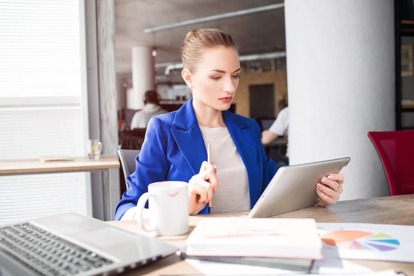 Smart och snygg kvinna sitter på bordet och ser att tabletten. Hon studerar. Flickan är mycket koncentrerad på ämne. — Stockfoto