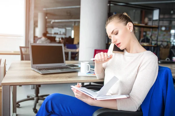 Flickan sitter i stol i sitt kontor och prata i telefon. Hon har ett telefon-möte. Ung kvinna är koncentrerad och allvarliga. — Stockfoto