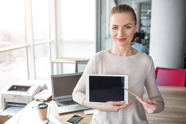 En bild av lycklig och glad kvinna med laptop i hennes händer. Hon har en penna i sin vänstra hand och show med det till skärmen tabletter. — Stockfoto