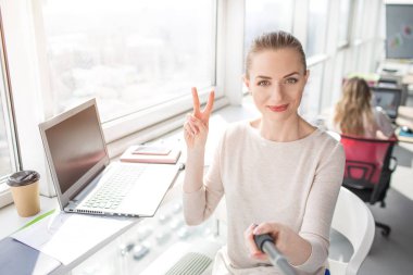 Burada güzel ofis çalışanı selfie alarak ve kamera parça sembole gösterilen farklı bir açıdan yapılmış bir resim. Çok mutlu ve memnun görünüyor.