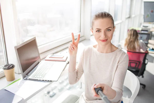 En bild som gjordes från en annan vinkel där vackra kontorsarbetare tar selfie och visar symbolen bit till kameran. Hon ser glad och nöjd. — Stockfoto