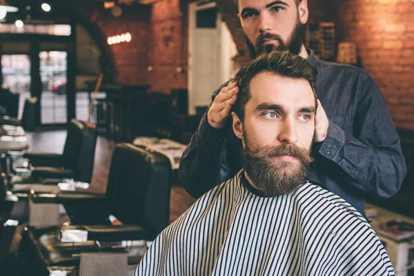 Przystojny facet jest odwrócił głowę w prawo przez fryzjerskiego. Hairdreser próbuje uzyskać dobra fryzura dla jego klienta. — Zdjęcie stockowe