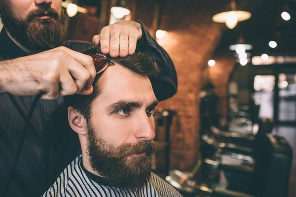 Fecha de perto um tipo barbudo. Seu cabeleireiro está cortando e modelando seu cabelo . — Fotografia de Stock