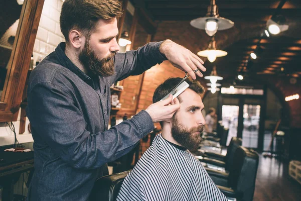 Outra foto de tipos barbudos na barbearia. Um homem está a cortar cabelo a outro homem. O procedimento é muito longo, mas intensivo . — Fotografia de Stock