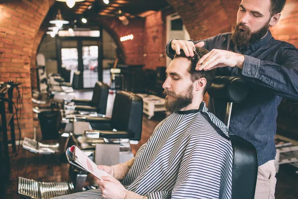 Klient siedzi w krzesło i czytania magazynu podczas gdy fryzjerka jest cięcie niektórych włosów. Robi to bardzo profesjonalny. — Zdjęcie stockowe