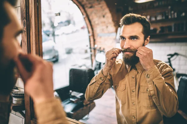 O homem feliz está a tocar no bigode com as duas mãos. Ele está orgulhoso disso. . — Fotografia de Stock