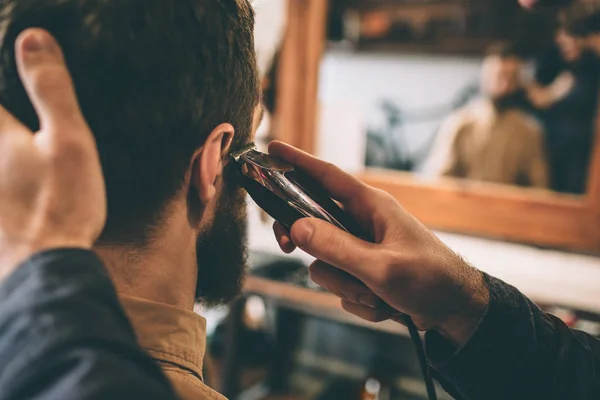 Wyciąć widok faceta cięcia włosów klienta z elektrycznych razer, w pobliżu prawego ucha. On trzyma głowę i robi to bardzo dokładne. — Zdjęcie stockowe