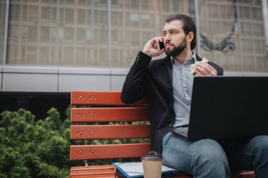 Meşgul bir adam acelesi var, o zaman yok, açık havada yemek yiyip bitirecek. Yeme ve belgelerle dizüstü bilgisayarda aynı anda çalışan işçi. Birden fazla görev yapıyor işadamı