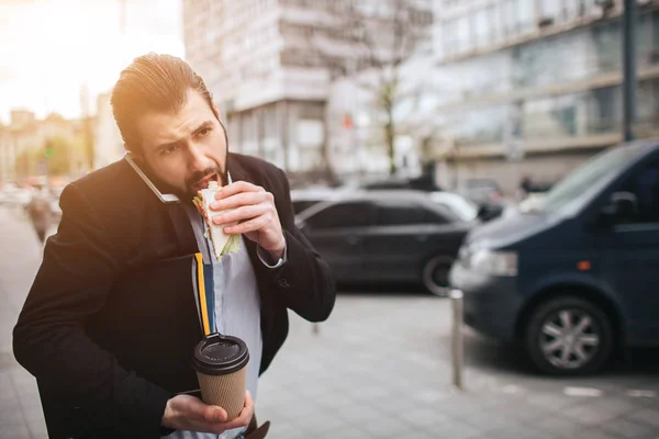 Busy man is in a hurry, he does not have time, he is going to eat snack on the go. Worker eating, drinking coffee, talking on the phone, at the same time. Businessman doing multiple tasks — Stock Photo, Image