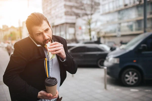 El hombre ocupado está apurado, no tiene tiempo, va a comer bocadillos sobre la marcha. Trabajador comiendo, bebiendo café, hablando por teléfono, al mismo tiempo. Empresario haciendo múltiples tareas — Foto de Stock