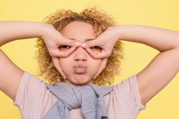 Ein Bild von lustigen Mädchen, die ihre Finger im Kreis halten und etwas Luft im Mund halten. sie sieht lustig, aber ernst aus. isoliert auf gelbem Hintergrund. — Stockfoto