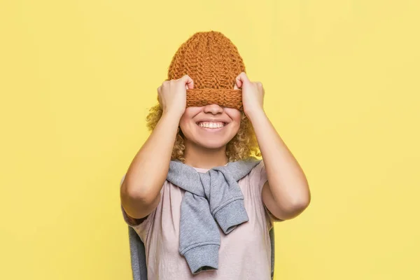 Glad tjej är stretching hatt ned. Hon har lagt det på hennes yeys och leende. Isolerad på gul bakgrund. — Stockfoto