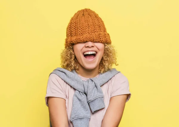 Fröhliches und positives Mädchen hat den braunen Hut auf ihre Augen gesetzt. Sie kann nichts sehen. Aber sie ist zufrieden. isoliert auf gelbem Hintergrund. — Stockfoto