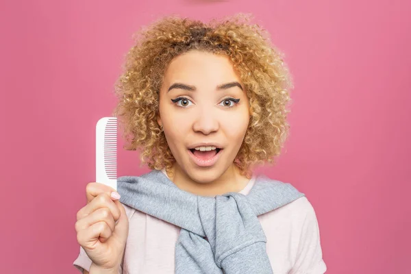 Portrait d'une fille aux cheveux bouclés. Elle tient une petite brosse blanche dans ses mains. La jeune femme regarde vers la caméra. Isolé sur fond rose . — Photo