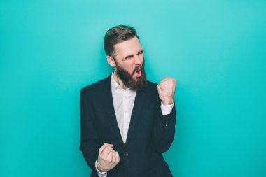 Yakışıklı adam sreaming mutluluk nedeniyle mı? Parmaklarını bir yumruk tutuyor. Üzerinde mavi arka plan izole.