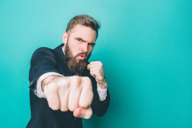 Another picture of strong guy in suite. He is showing his right fist to the camera. Thia man looks serious and brutal. Isolated on blue background. clipart