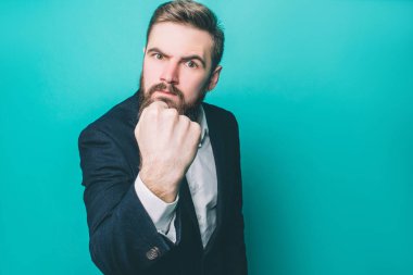 Ciddi ve acımasız adam yumruğunu kamera için gösteriyor. Adam kızgın. Duygularını saklamıyor. Üzerinde mavi arka plan izole.