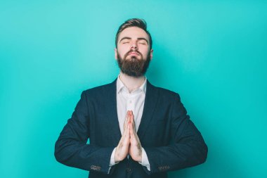 Ciddi adam dua bir resim. Onun el ele tutusun ve gözleri kapalı tutuyor. Üzerinde mavi arka plan izole.