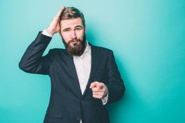 Suite güzel ve yakışıklı adam ayakta ve poz. O saçları çok dokunaklı ve kamera işaret. Adam çok emindir. Üzerinde mavi arka plan izole.