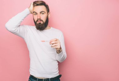 Hayret adamın elinde bir hamilelik testi var. Ne yapacağını bilmiyor. Pembe arka plan izole.
