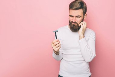 Sinirli adam bir razer tutuyor ve ne yapacağını bilmiyor. O yanak dokunmadan ve düşünüyor. Pembe arka plan izole.