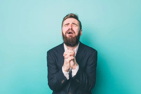 Guy is standing and holding his hands together. He is praying and begging. Also he is yelling. Isolated on blue background. — Stock Photo, Image