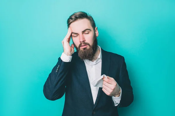 Man håller handen på huvudet. Han har huvudvärk. Kille lider av den. Han har också en servett i höger hand. Isolerad på blå bakgrund. — Stockfoto