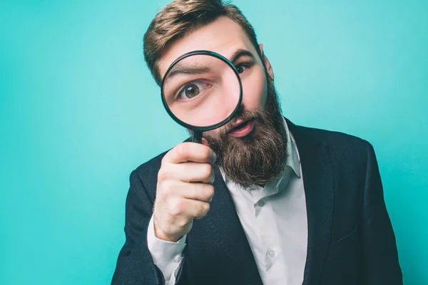 Strange man is looking straight through the loupe. He wonders. Isolated on blue background. — Stock Photo, Image