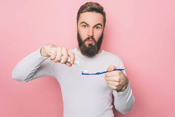 Förvånade är att sätta lite tandkräm på en tandborste. Han bryr sig om sin hälsa. Man ser rakt fram. Isolerad på rosa bakgrund. — Stockfoto