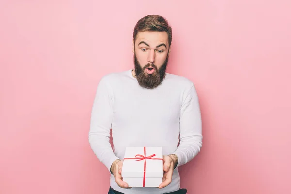 Förvånad killen är ständiga och hålla en present. Rutan är vit med rött band. Isolerad på rosa bakgrund. — Stockfoto