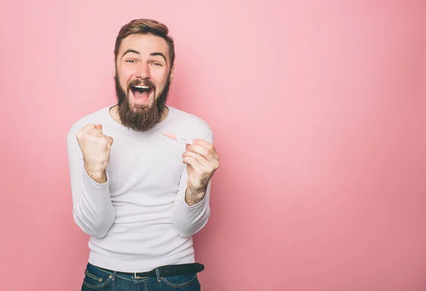 Happy guy is screaming. He has a pregnancy test in his hands. Isolated on pink background. — Stock Photo, Image