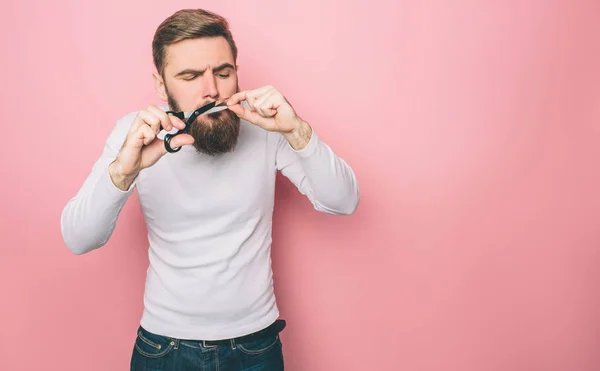 En bild av killen skära sin mustasch med saxen. Han gör det mycket exakt. Isolerad på rosa bakgrund. — Stockfoto