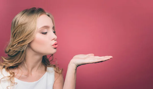 Hübsche junge Frau posiert. Sie hat die Augen geschlossen und ihre Lippen zu einem Kuss zusammengelegt. Sie schickt ein paar Küsse. isoliert auf rosa Hintergrund. — Stockfoto