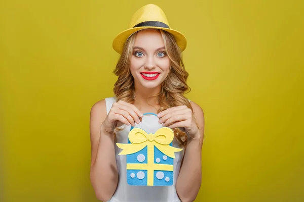 Überraschtes Mädchen hält ein Geschenk in den Händen. Sie blickt geradeaus und lächelt. isoliert auf gelbem Hintergrund. — Stockfoto