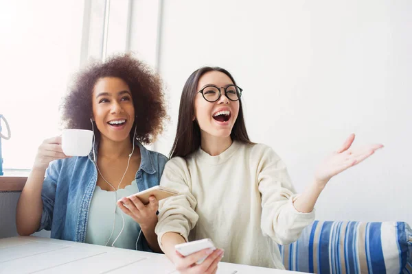 Glückliche Studenten sitzen auf dem Sofa. Mädchen im weißen Pullover zeigt ihre Anzeige in der linken Hand, während ihr Freund Tee trinkt und lächelt. — Stockfoto