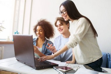 Asyalı kız ayakta ve klavyede elini tutarak. Bir adam ve başka bir kız kanepede oturan ve de laptop arıyorum.