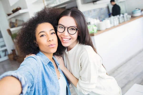Selfie van twee mooie vrienden samen staan. Afro-Amerikaanse houdt een telefoon in haar handen terwijl de andere een gewoon naar haar vriend leunt. — Stockfoto