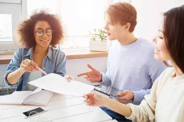 Los estudiantes están resolviendo el problema. Están estudiando. Las niñas están sosteniendo un pedazo de papel mientras la chica de camisa azul y un chico están mostrando al papel . — Foto de Stock